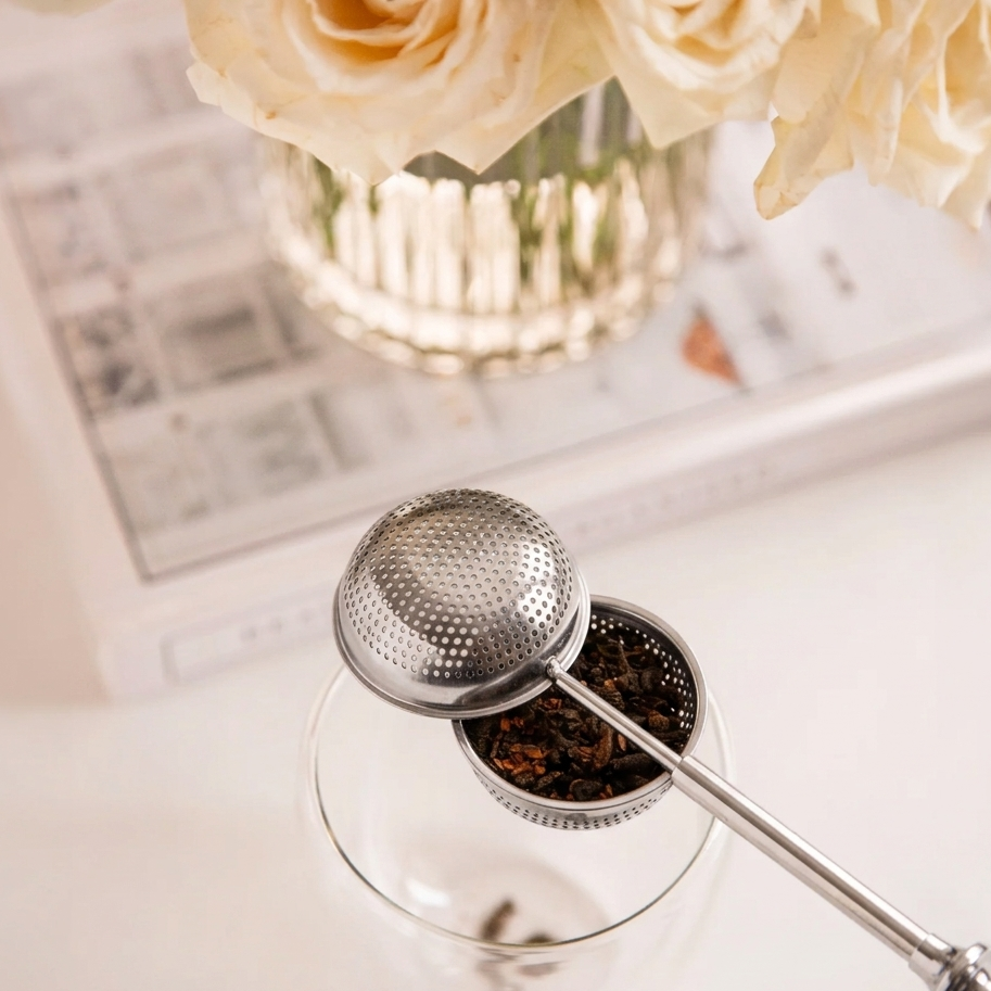Human hands using wooden scoop to fill open LittleCalm stainless steel mesh tea infuser.